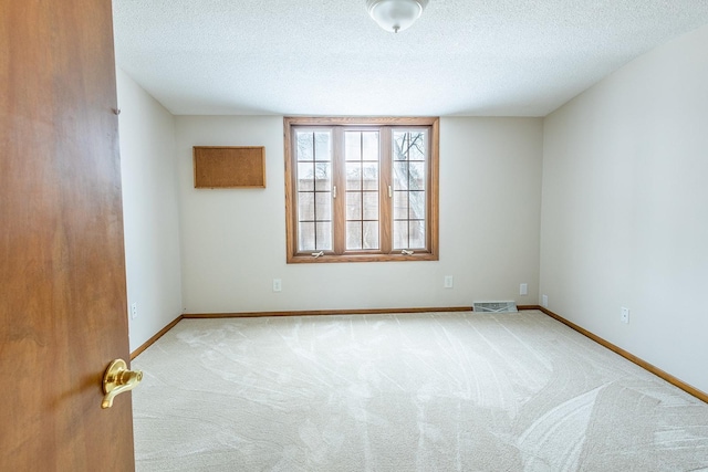 empty room featuring carpet floors, visible vents, a textured ceiling, and baseboards