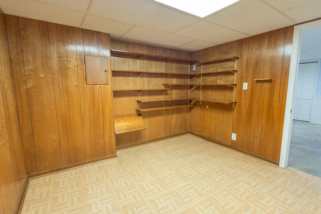 interior space featuring parquet floors, a drop ceiling, wooden walls, and baseboards