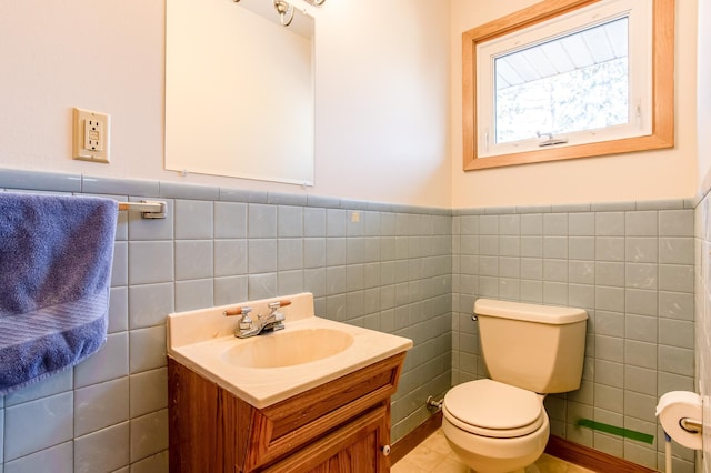 half bath with toilet, tile walls, wainscoting, and vanity