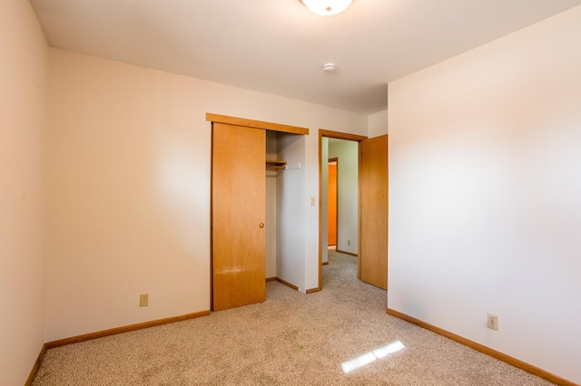 unfurnished bedroom with light carpet, a closet, and baseboards