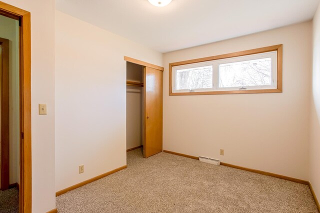 unfurnished bedroom with a baseboard radiator, light colored carpet, a closet, and baseboards