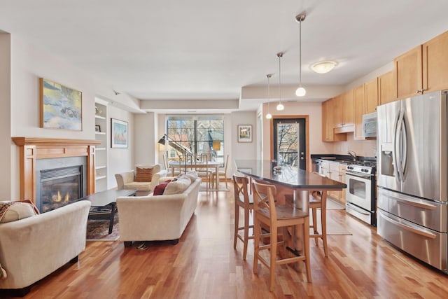 kitchen with dark countertops, a premium fireplace, stainless steel appliances, light brown cabinetry, and pendant lighting