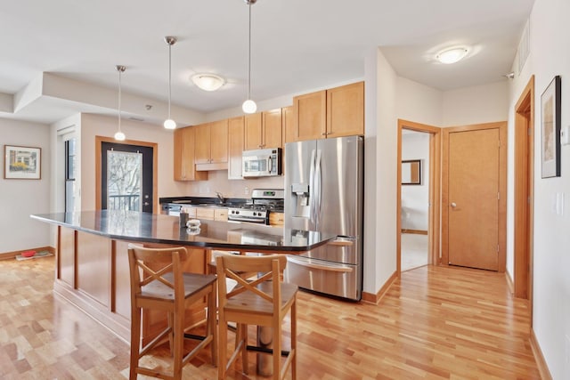 kitchen with stainless steel appliances, a kitchen island, dark countertops, a kitchen bar, and decorative light fixtures