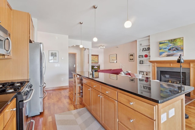 kitchen featuring open floor plan, appliances with stainless steel finishes, a center island, light wood finished floors, and pendant lighting