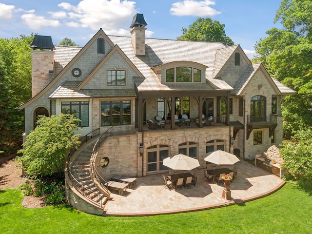 back of house featuring a patio, a chimney, stairway, a balcony, and stone siding