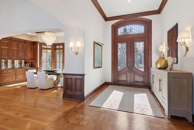 foyer with arched walkways, french doors, ornamental molding, a chandelier, and baseboards