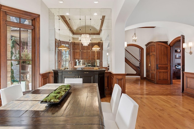 dining space featuring arched walkways, a wainscoted wall, light wood-style floors, stairs, and an inviting chandelier