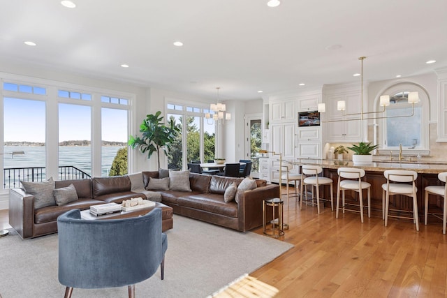 living room featuring recessed lighting, light wood-type flooring, a water view, and a notable chandelier