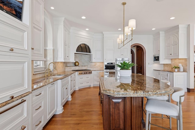 kitchen featuring light wood finished floors, arched walkways, a breakfast bar area, stainless steel gas stovetop, and a sink