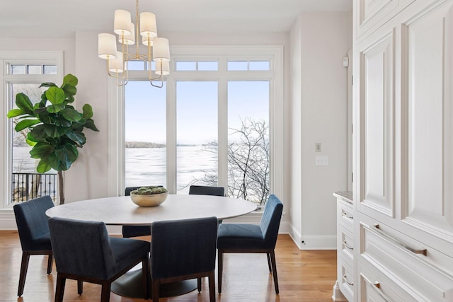 dining space with a water view, light wood-style floors, baseboards, and a notable chandelier