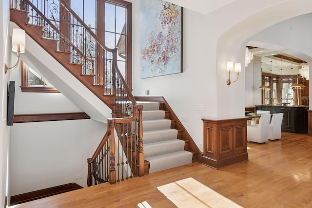 stairs with arched walkways, wood finished floors, and a wealth of natural light