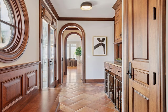 foyer featuring light tile patterned floors, baseboards, ornamental molding, and arched walkways