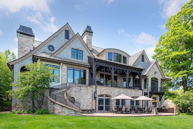 rear view of house with a yard, a patio, a balcony, stone siding, and stairs