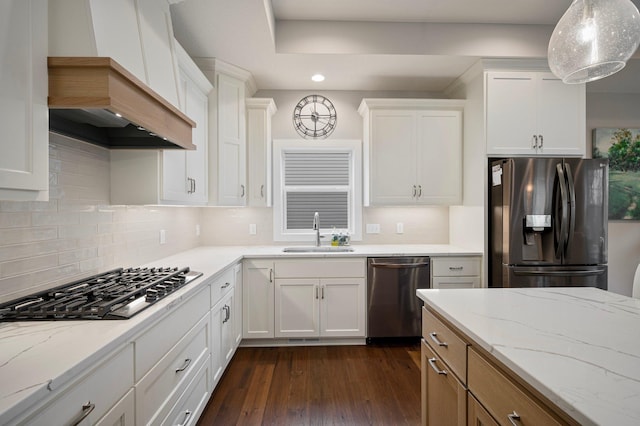 kitchen with white cabinets, custom range hood, hanging light fixtures, stainless steel appliances, and a sink