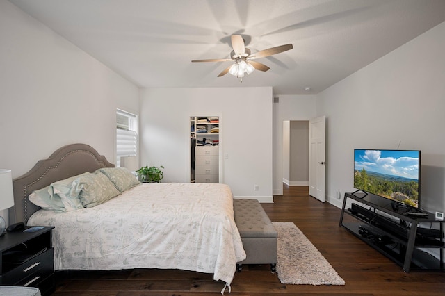 bedroom with dark wood-style flooring, ceiling fan, a spacious closet, and baseboards