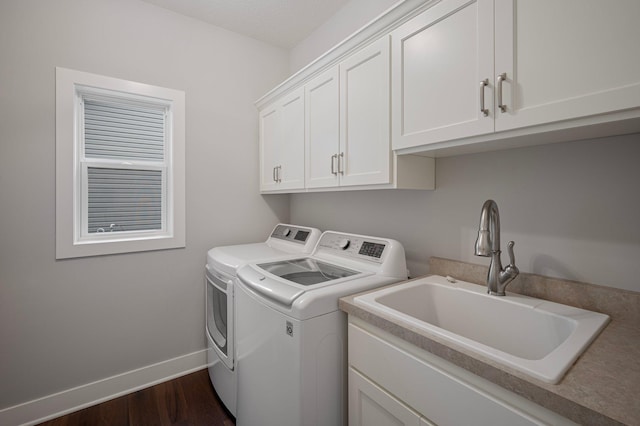 washroom featuring a sink, baseboards, cabinet space, dark wood-style floors, and washing machine and clothes dryer