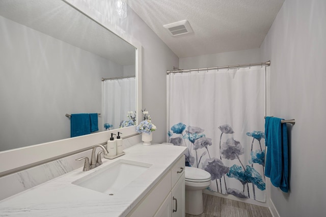 bathroom featuring visible vents, toilet, vanity, and a textured ceiling