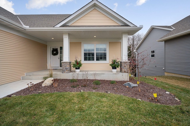 doorway to property featuring covered porch, a lawn, and roof with shingles