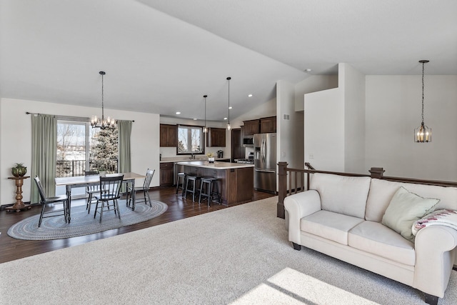 living area featuring dark wood finished floors, a healthy amount of sunlight, an inviting chandelier, and vaulted ceiling