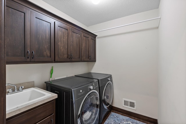 laundry room featuring visible vents, washing machine and dryer, cabinet space, a textured ceiling, and a sink