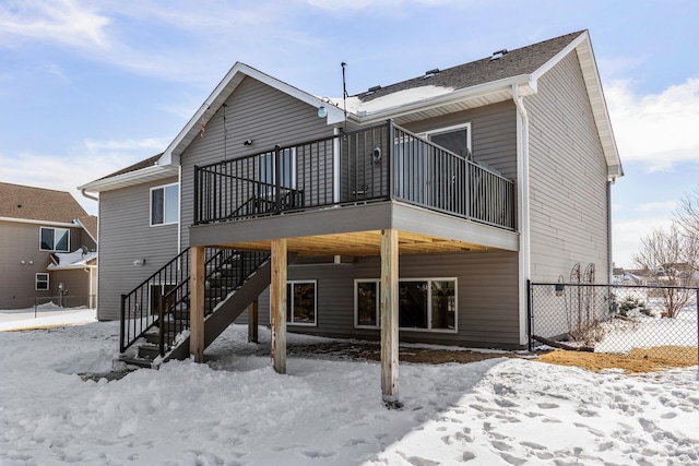 snow covered house with stairs, fence, and a wooden deck