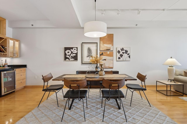 dining room with light wood finished floors, wine cooler, a dry bar, and baseboards