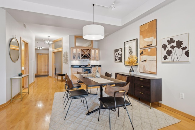 dining area featuring rail lighting, baseboards, light wood-style flooring, and a bar