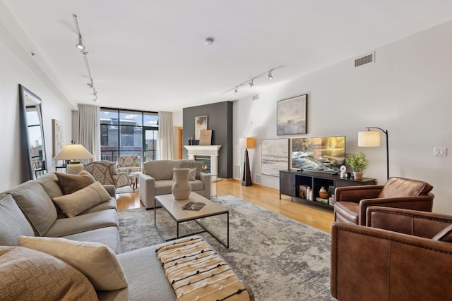 living area featuring visible vents, light wood-style flooring, a glass covered fireplace, track lighting, and a wall of windows