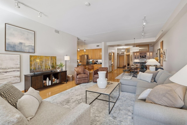 living area featuring rail lighting, visible vents, and light wood-style floors