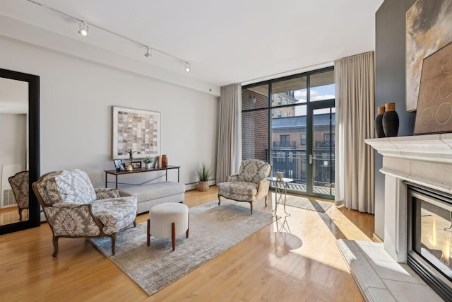 living room featuring light wood-type flooring, a glass covered fireplace, rail lighting, and floor to ceiling windows