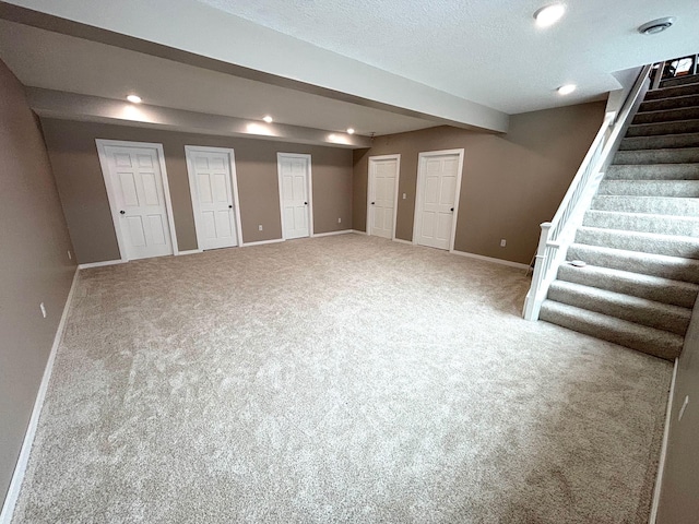 finished below grade area with a textured ceiling, recessed lighting, carpet floors, baseboards, and stairway