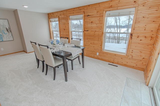 dining room featuring visible vents, light carpet, wooden walls, and baseboards