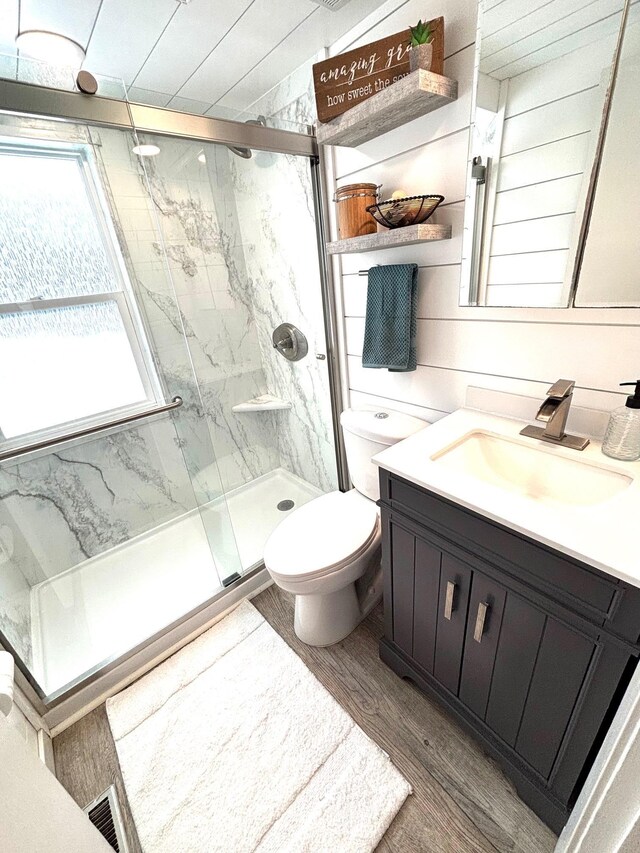 bathroom with a marble finish shower, visible vents, toilet, wood finished floors, and vanity