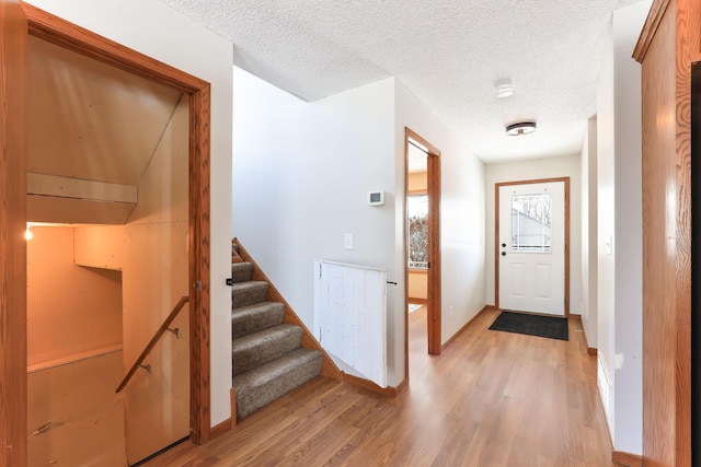 entrance foyer with light wood-style floors, stairway, baseboards, and a textured ceiling