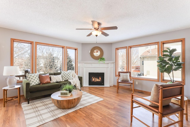 living area with a textured ceiling, a fireplace, a ceiling fan, and light wood-style floors