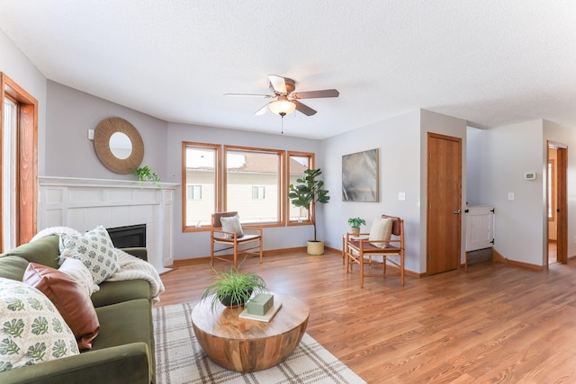 living room with light wood-style flooring, ceiling fan, a textured ceiling, and a tile fireplace