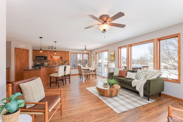 living room with light wood-type flooring, ceiling fan, a textured ceiling, and baseboards