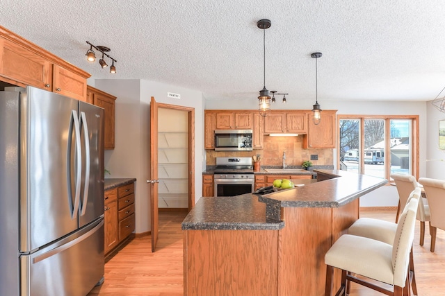 kitchen featuring appliances with stainless steel finishes, dark countertops, hanging light fixtures, and a sink