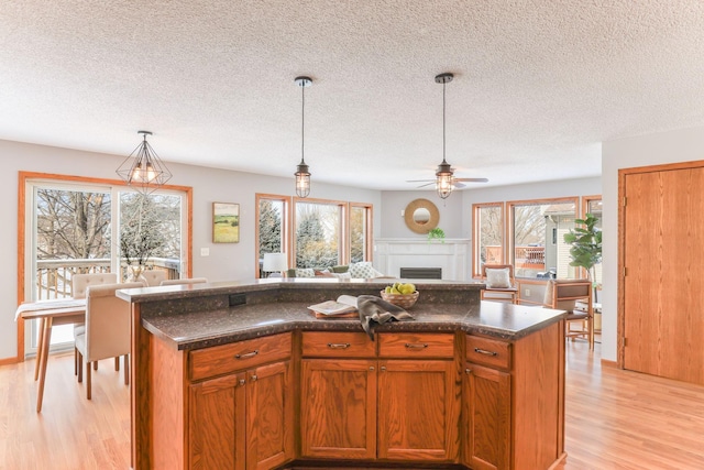 kitchen with brown cabinets, open floor plan, hanging light fixtures, light wood-style floors, and a fireplace