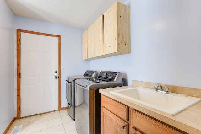 clothes washing area with cabinet space, light tile patterned flooring, a sink, a textured ceiling, and washer and dryer