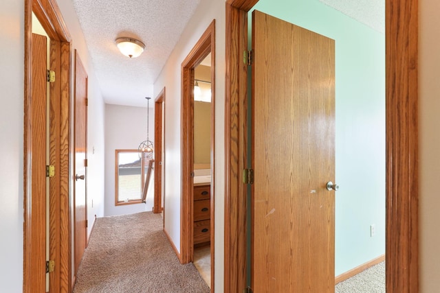 corridor with a textured ceiling, baseboards, and light colored carpet