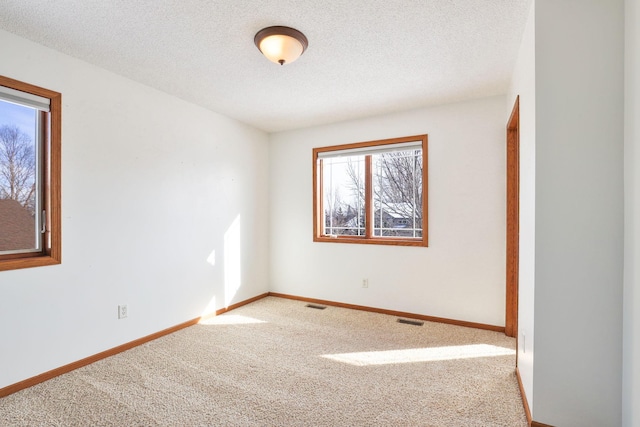 carpeted empty room featuring a textured ceiling, visible vents, and baseboards