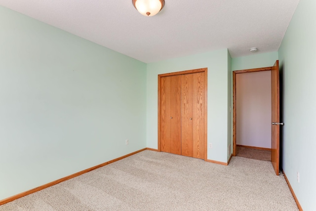 unfurnished bedroom featuring light carpet, a closet, a textured ceiling, and baseboards