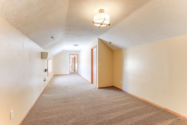 additional living space with vaulted ceiling, a textured ceiling, carpet flooring, and baseboards