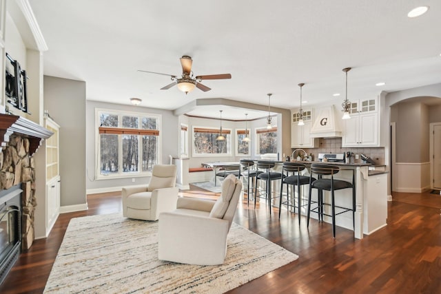 living room featuring baseboards, arched walkways, a ceiling fan, dark wood-style floors, and a fireplace