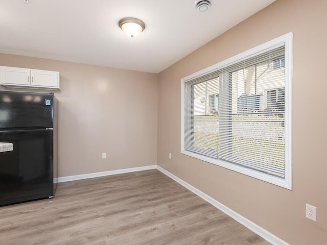 kitchen with freestanding refrigerator, white cabinets, light wood-style flooring, and baseboards