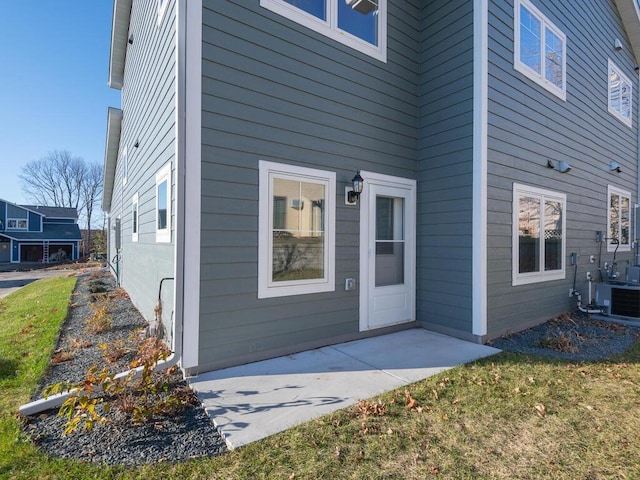 entrance to property featuring central AC unit, a lawn, and a patio