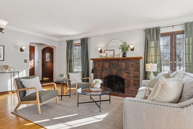 living room featuring light wood finished floors, a brick fireplace, arched walkways, and crown molding