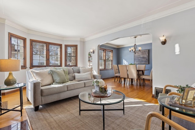 living room featuring visible vents, arched walkways, light wood-style flooring, ornamental molding, and a chandelier