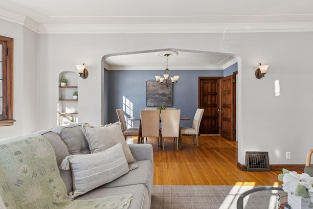 living room with arched walkways, crown molding, visible vents, light wood-style flooring, and a chandelier